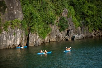 Tourists kayaking along the lush limestone cliffs of Ha Long Bay, enjoying the natural beauty and adventure offered by Peony Cruise