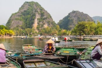 Traditional rowing boats on a river in Ninh Binh with limestone mountains in the background and people wearing conical hats